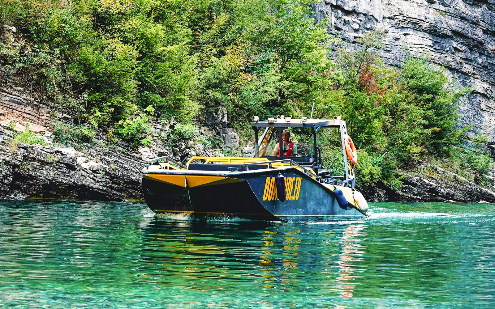 Boat navigating Komani Lake with lush cliffs in the background during Tirana day trip.