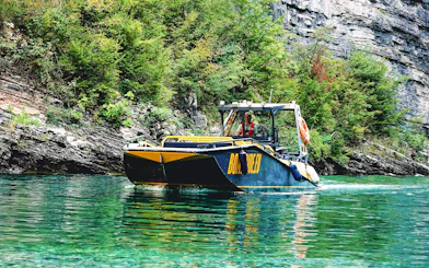 Boat navigating Komani Lake with lush cliffs in the background during Tirana day trip.
