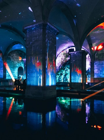Immersive light show in an underground vaulted space with colorful projections.