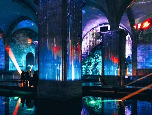 Immersive light show in an underground vaulted space with colorful projections.