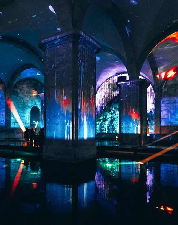 Immersive light show in an underground vaulted space with colorful projections.