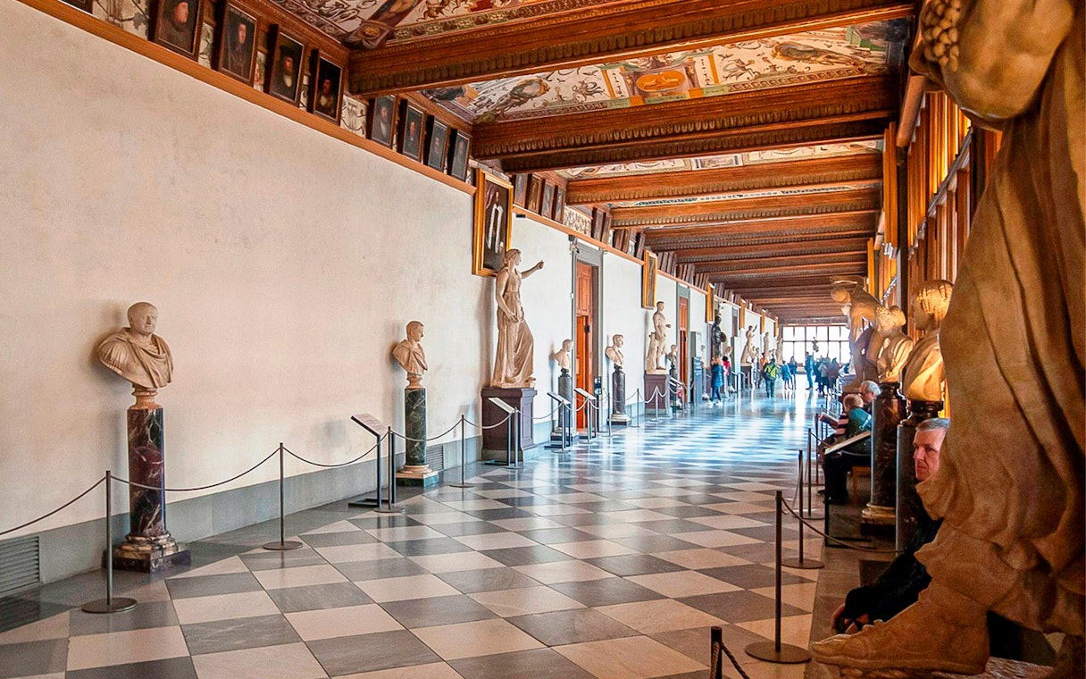 Uffizi Gallery corridor with classical sculptures and visitors in Florence, Italy.