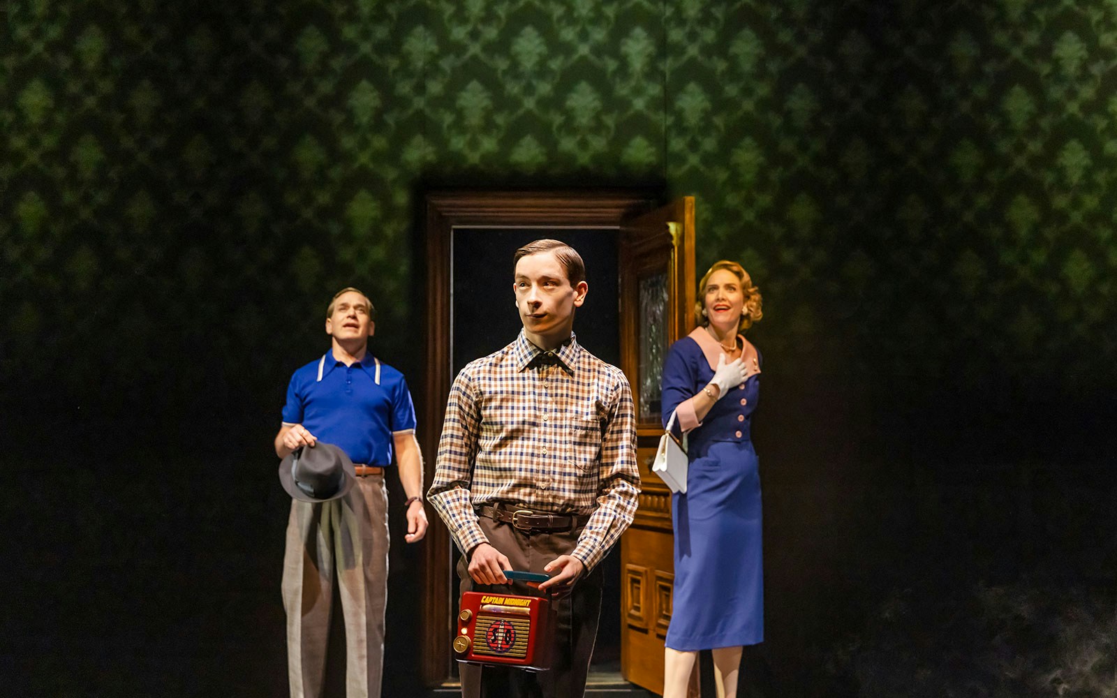 Three people in vintage attire stand in a dimly lit room, one holding a retro radio.