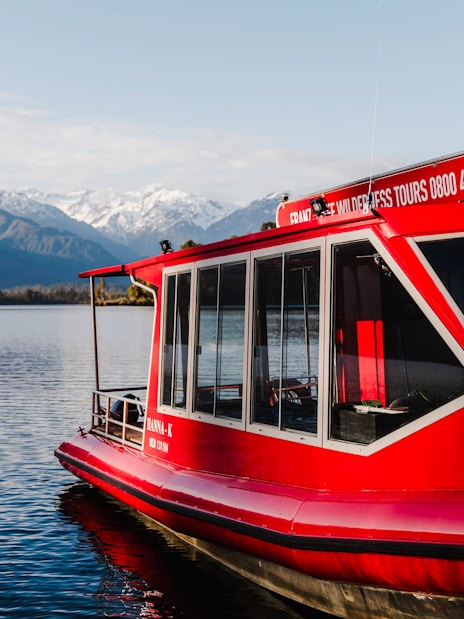 Red tour boat on Lake Mapourika with snow-capped mountains in the background.