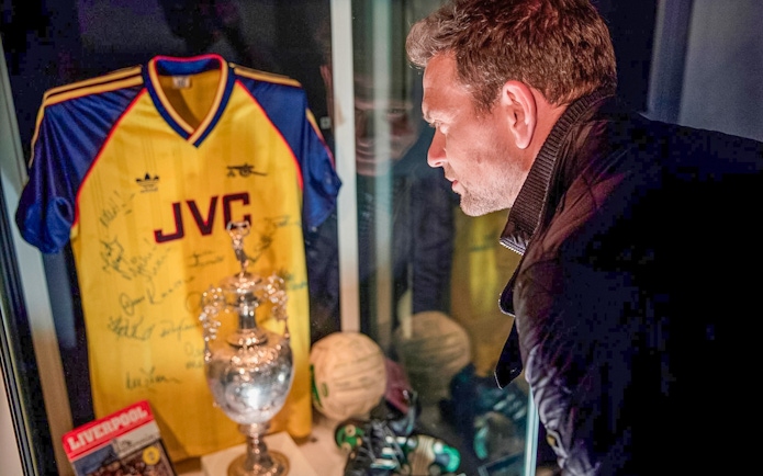 Man viewing Arsenal FC memorabilia display with signed jersey and trophy at Emirates Stadium.