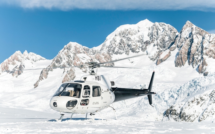 Helicopter on snow at Fox Glacier with mountain backdrop, Franz Josef tour.