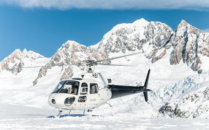Helicopter on snow at Fox Glacier with mountain backdrop, Franz Josef tour.