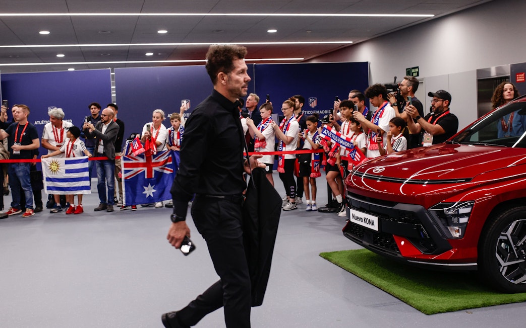 Atletico Madrid manager entering stadium with fans holding flags and taking photos.