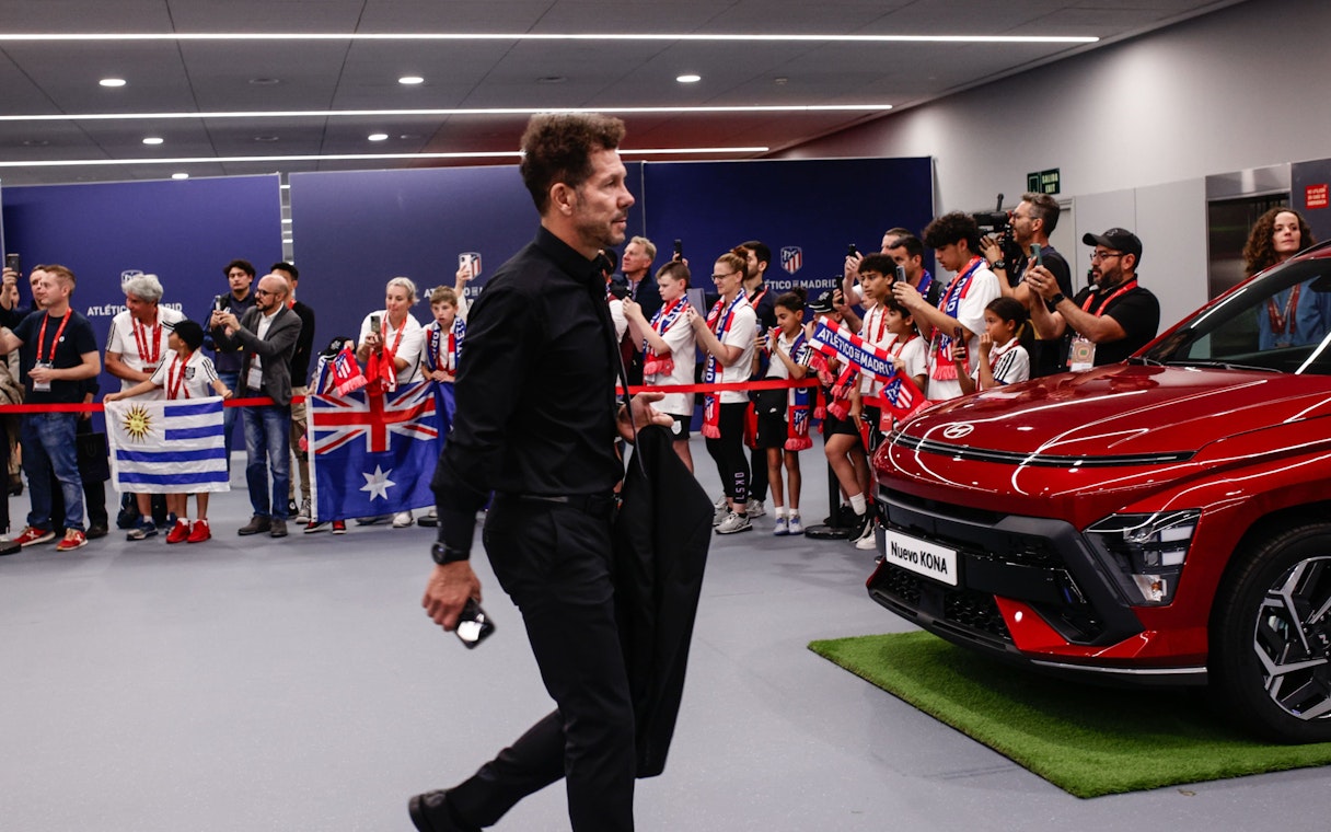 Atletico Madrid manager entering stadium with fans holding flags and taking photos.