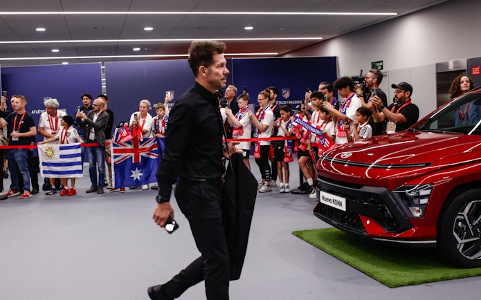 Atletico Madrid manager entering stadium with fans holding flags and taking photos.