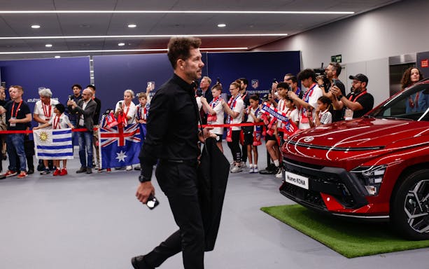 Atletico Madrid manager entering stadium with fans holding flags and taking photos.