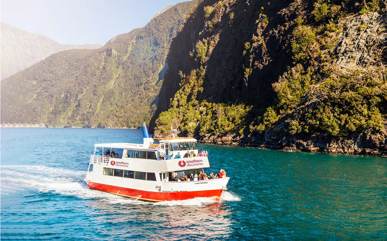 Cruise boat on Milford Sound with scenic cliffs, Te Anau tour.