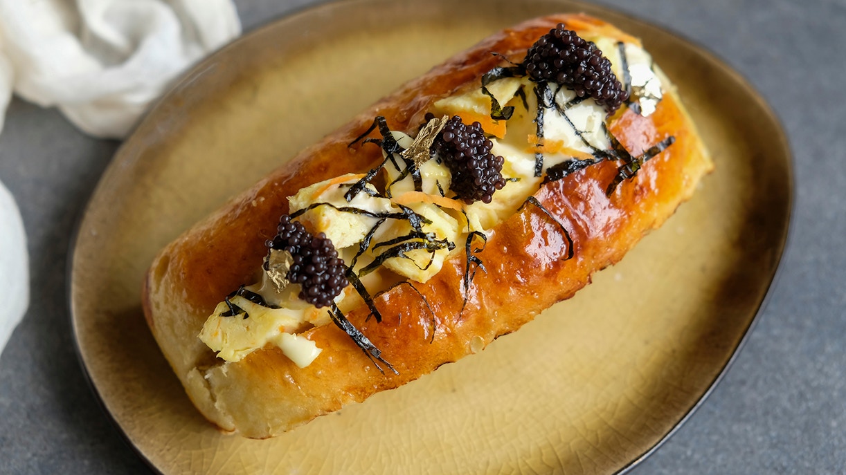 Caviar-topped brioche with seaweed and cheese on a plate.