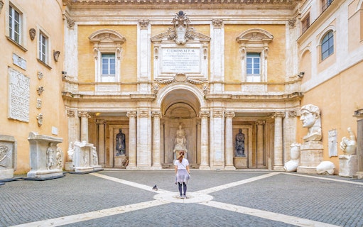 Girl standing in courtyard of Capitoline Museum, Rome, surrounded by ancient sculptures.