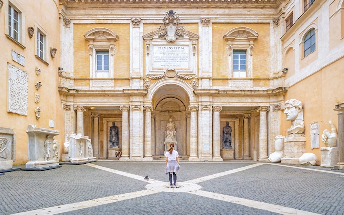 Girl standing in courtyard of Capitoline Museum, Rome, surrounded by ancient sculptures.