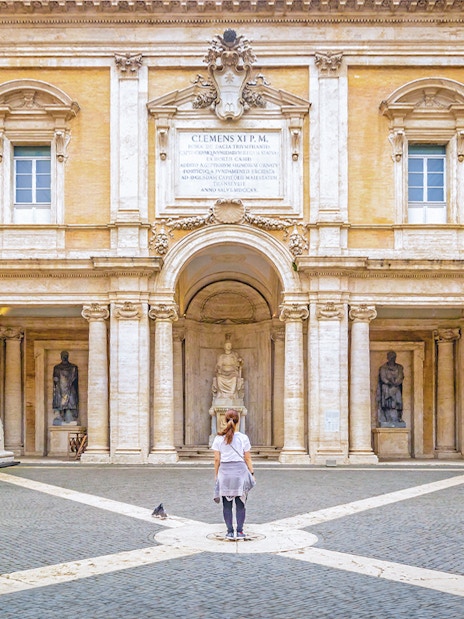 Girl standing in courtyard of Capitoline Museum, Rome, surrounded by ancient sculptures.