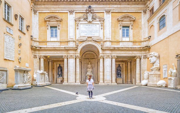 Girl standing in courtyard of Capitoline Museum, Rome, surrounded by ancient sculptures.