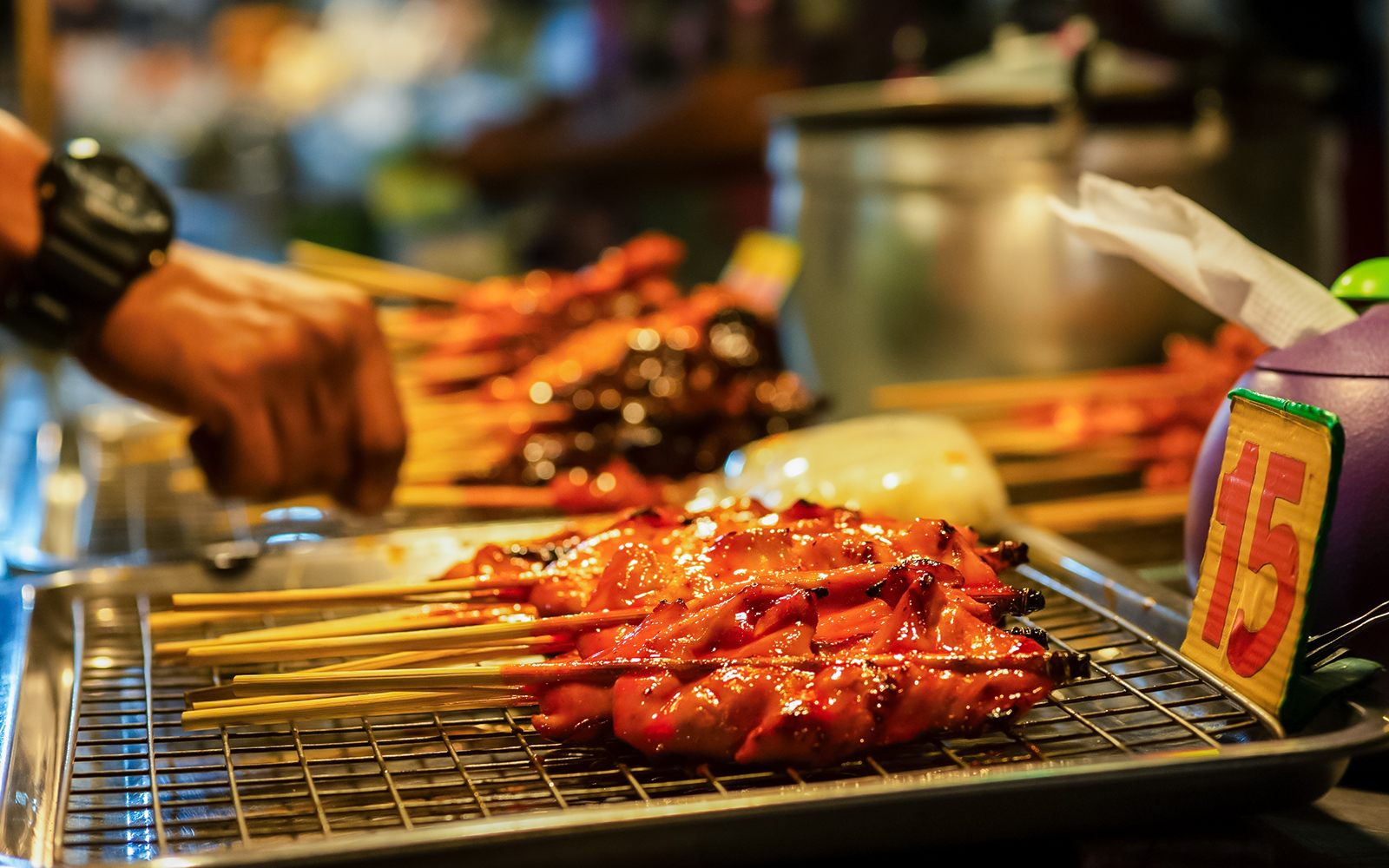 Pattaya Night Market vendor preparing street food skewers on a grill.