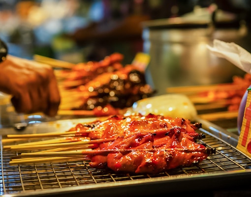 Pattaya Night Market vendor preparing street food skewers on a grill.