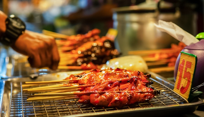 vendor preparing street food skewers on a grill.