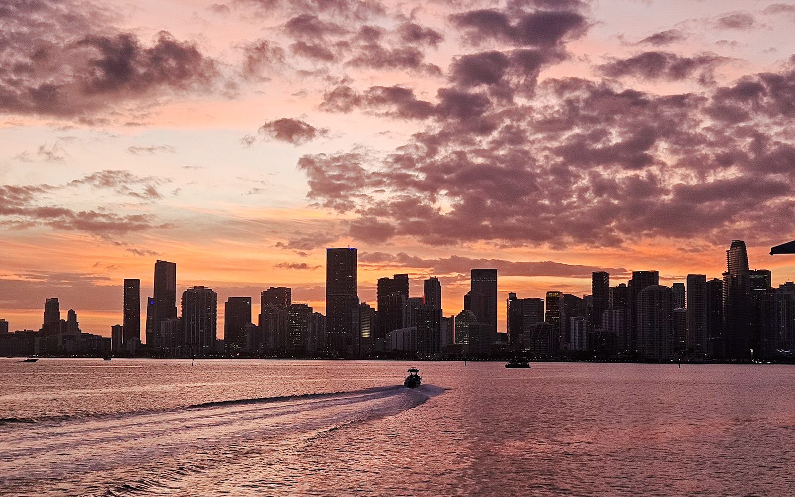 Miami skyline at sunset with a boat cruising on the water.