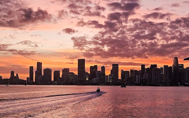 Miami skyline at sunset with a boat cruising on the water.