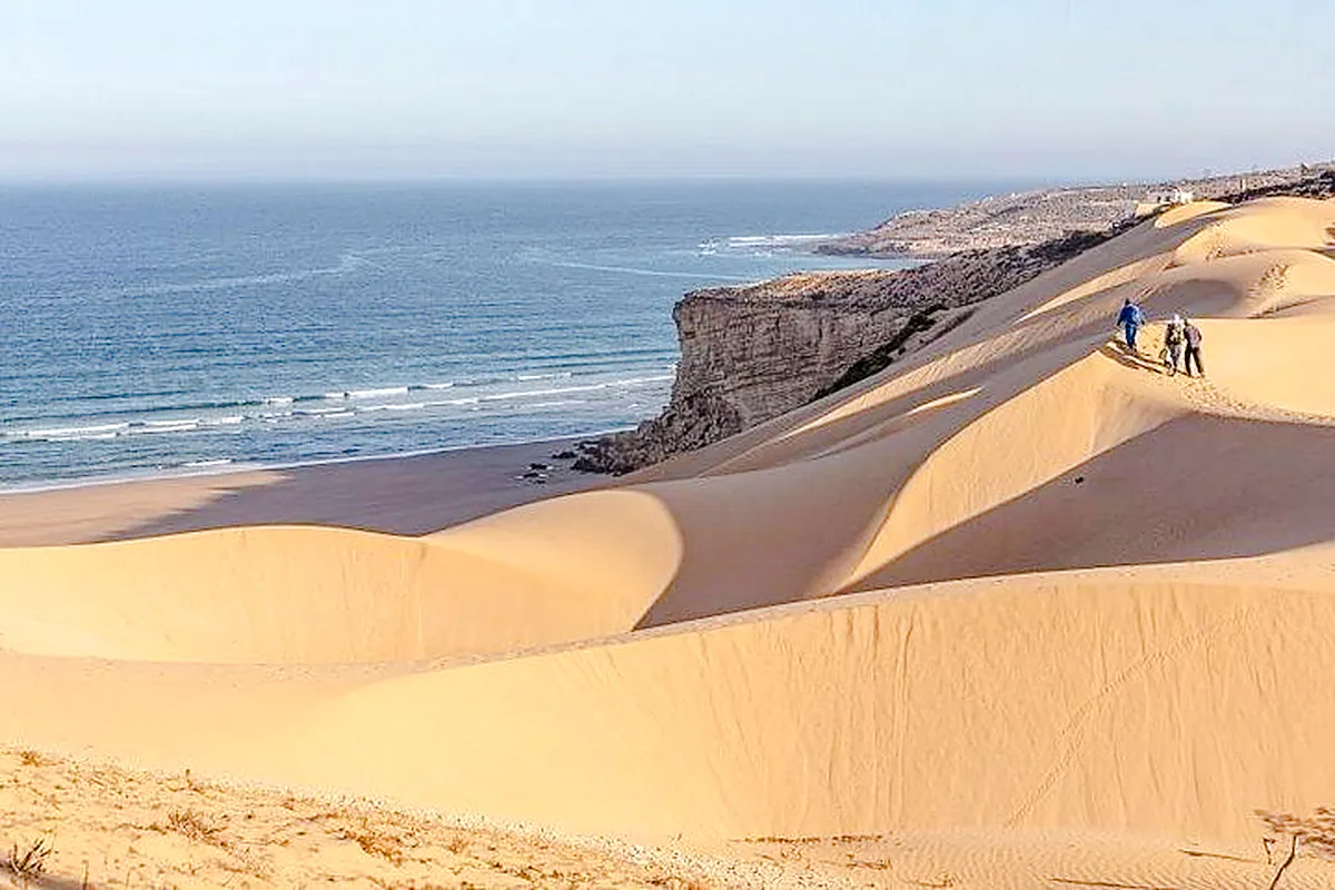 Jeep safari group walking on sand dunes near ocean cliffs, Agadir.