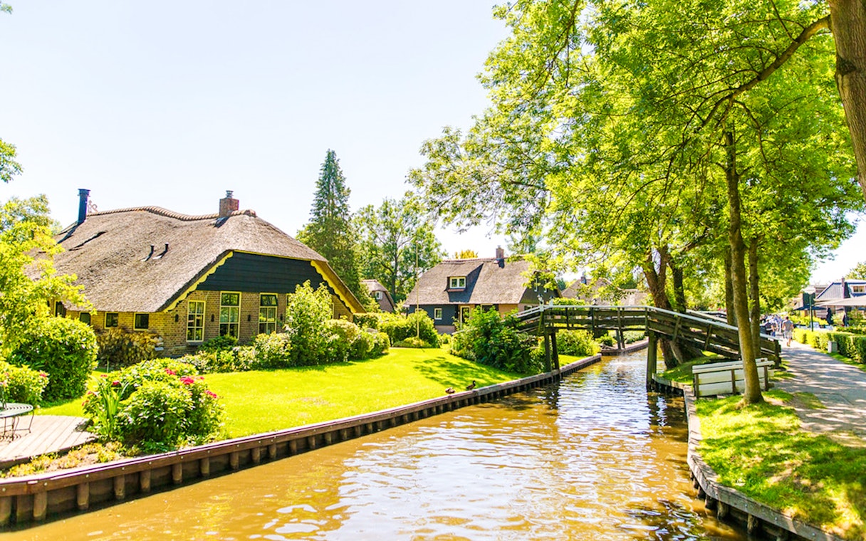 Canal view with thatched-roof houses and wooden bridge in Giethoorn, Netherlands.