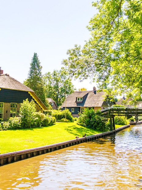 Canal view with thatched-roof houses and wooden bridge in Giethoorn, Netherlands.