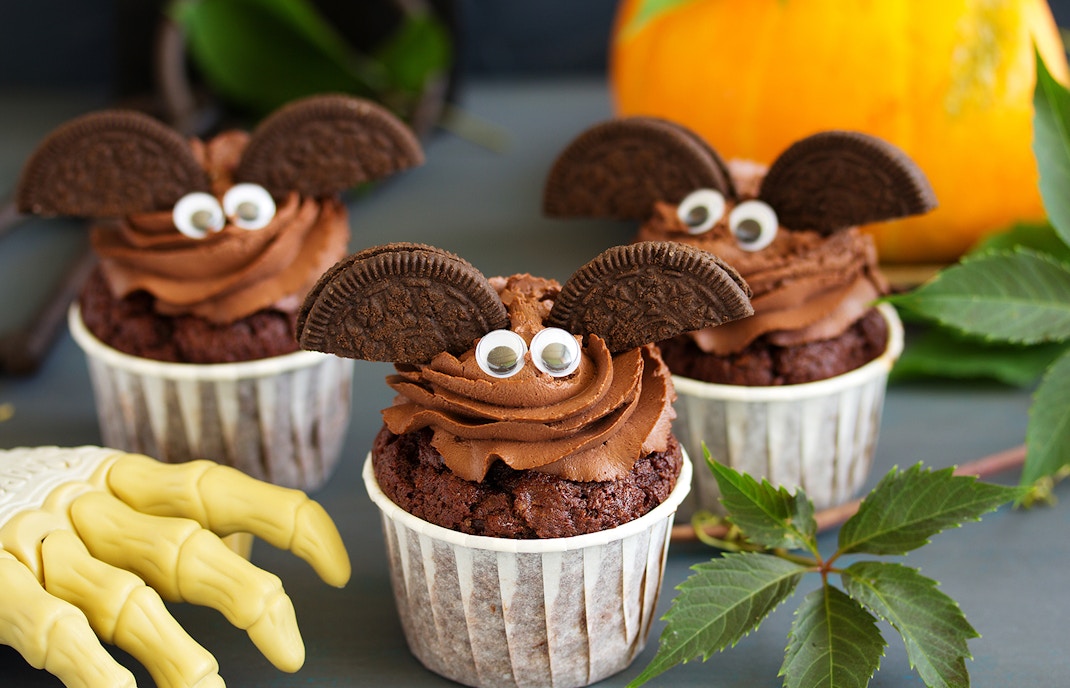 Chocolate cupcakes decorated as bats with cookie wings and candy eyes, Halloween theme.