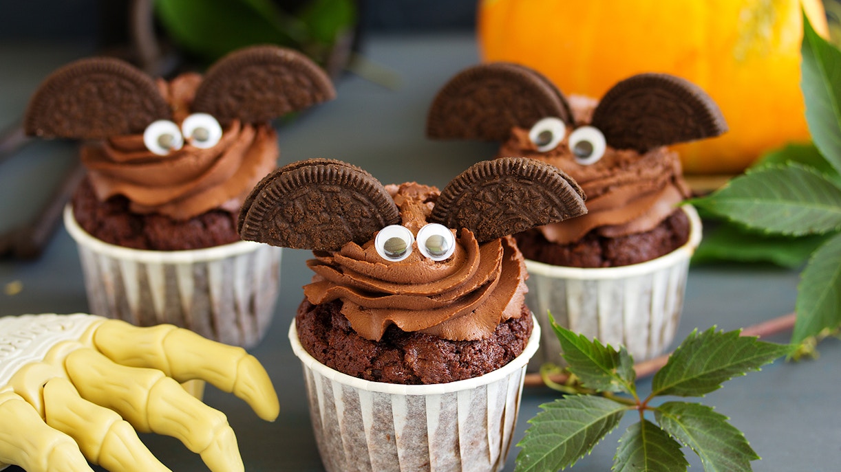 Chocolate cupcakes decorated as bats with cookie wings and candy eyes, Halloween theme.