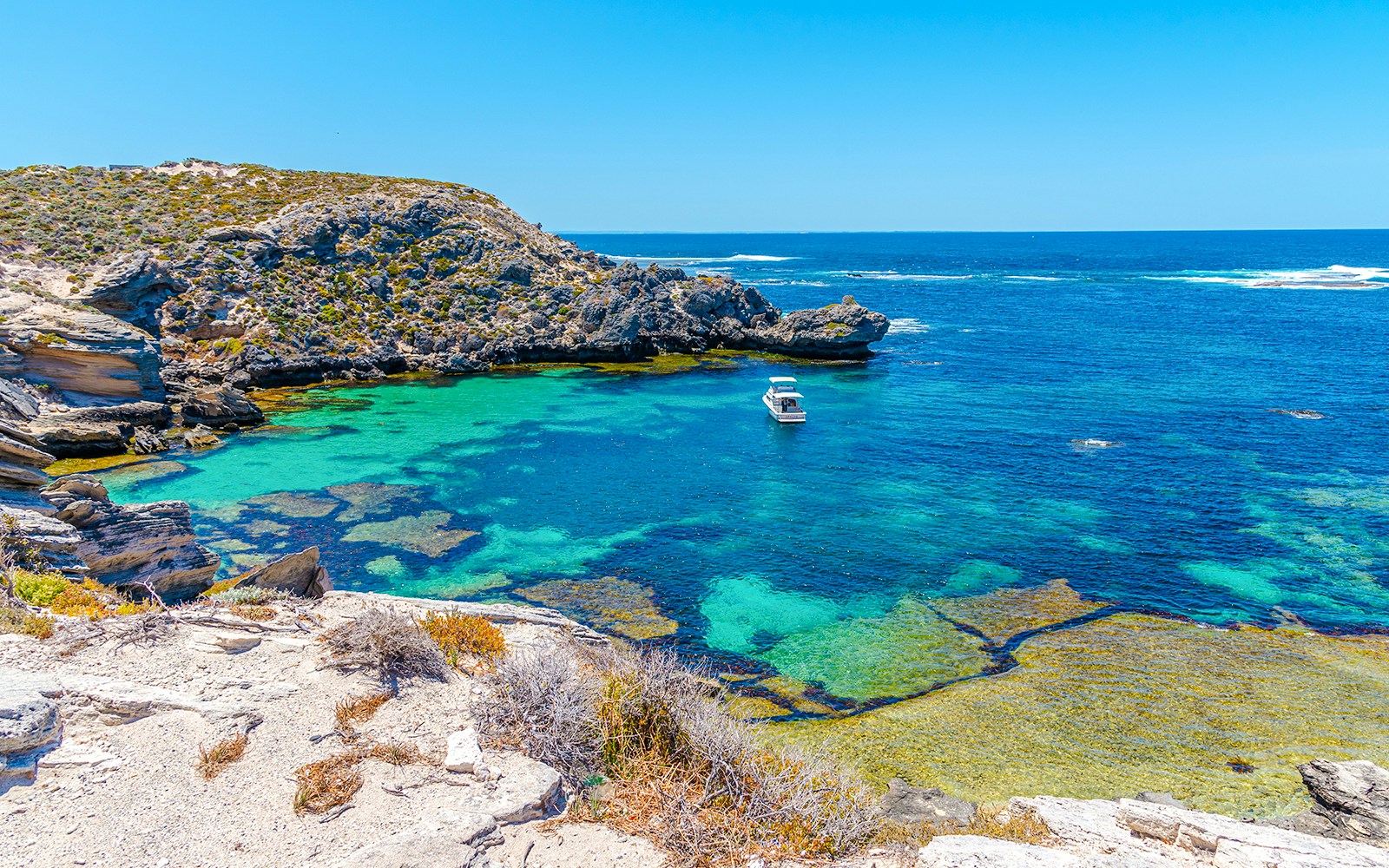 Boat in turquoise waters of Fish Hook Bay, Rottnest Island, with rocky coastline.