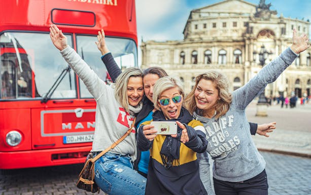 Group taking a selfie in front of a red tour bus in Dresden, Germany.