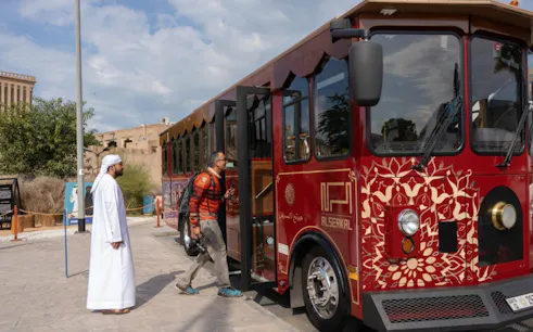 Man boarding a decorated trolley in Dubai with Emirati storyteller nearby.