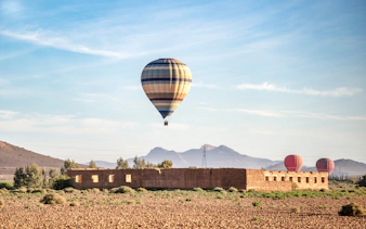 Hot air balloon over Berber village landscape, Marrakech, with mountains in the background.