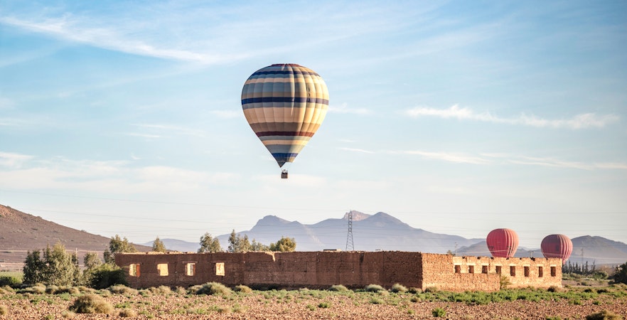 Hot air balloon over Berber village landscape, Marrakech, with mountains in the background.