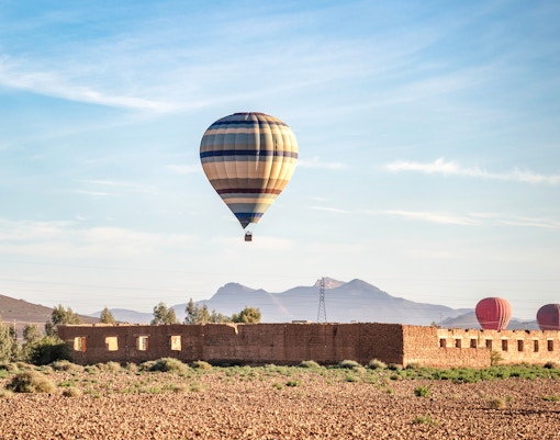 Hot air balloon over Berber village landscape, Marrakech, with mountains in the background.