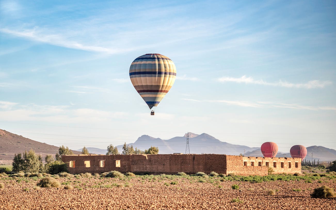 Hot air balloon over Berber village landscape, Marrakech, with mountains in the background.