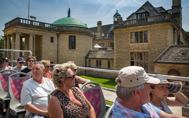 Tourists on an open-top bus tour in Oxford, viewing historic architecture.