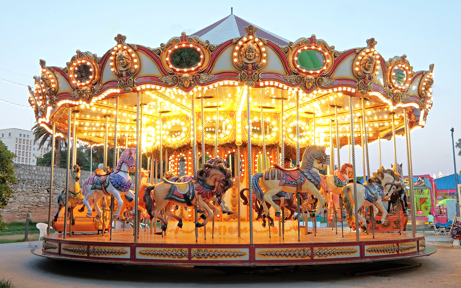 Carousel with illuminated horses at a theme park during evening.