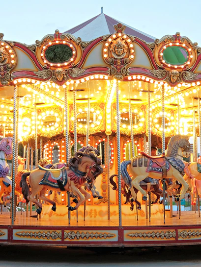 Carousel with illuminated horses at a theme park during evening.