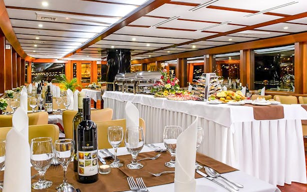 Cruise dining room with elegantly set tables and buffet spread.