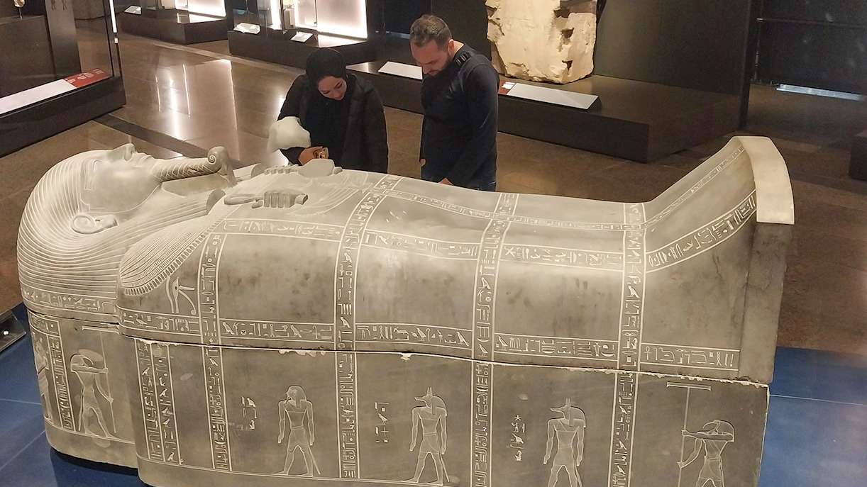 Visitors examining an ancient Egyptian sarcophagus at the Grand Egyptian Museum.