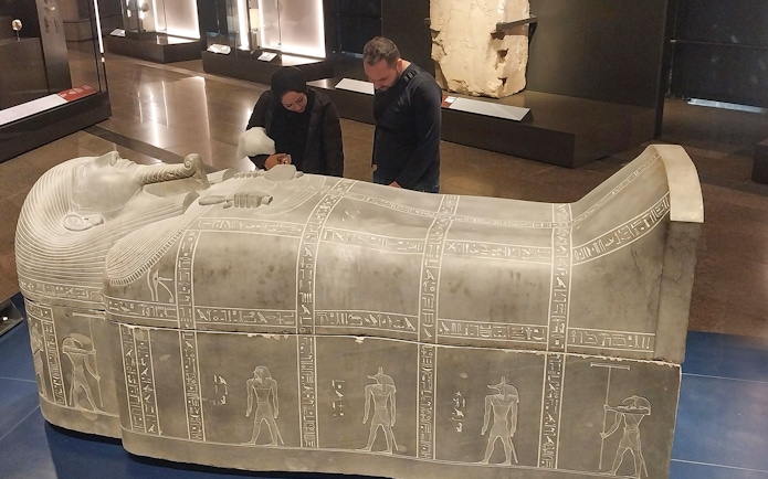 Visitors examining an ancient Egyptian sarcophagus at the Grand Egyptian Museum.