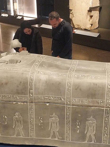 Visitors examining an ancient Egyptian sarcophagus at the Grand Egyptian Museum.