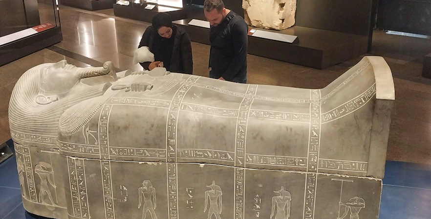 Visitors examining an ancient Egyptian sarcophagus at the Grand Egyptian Museum.