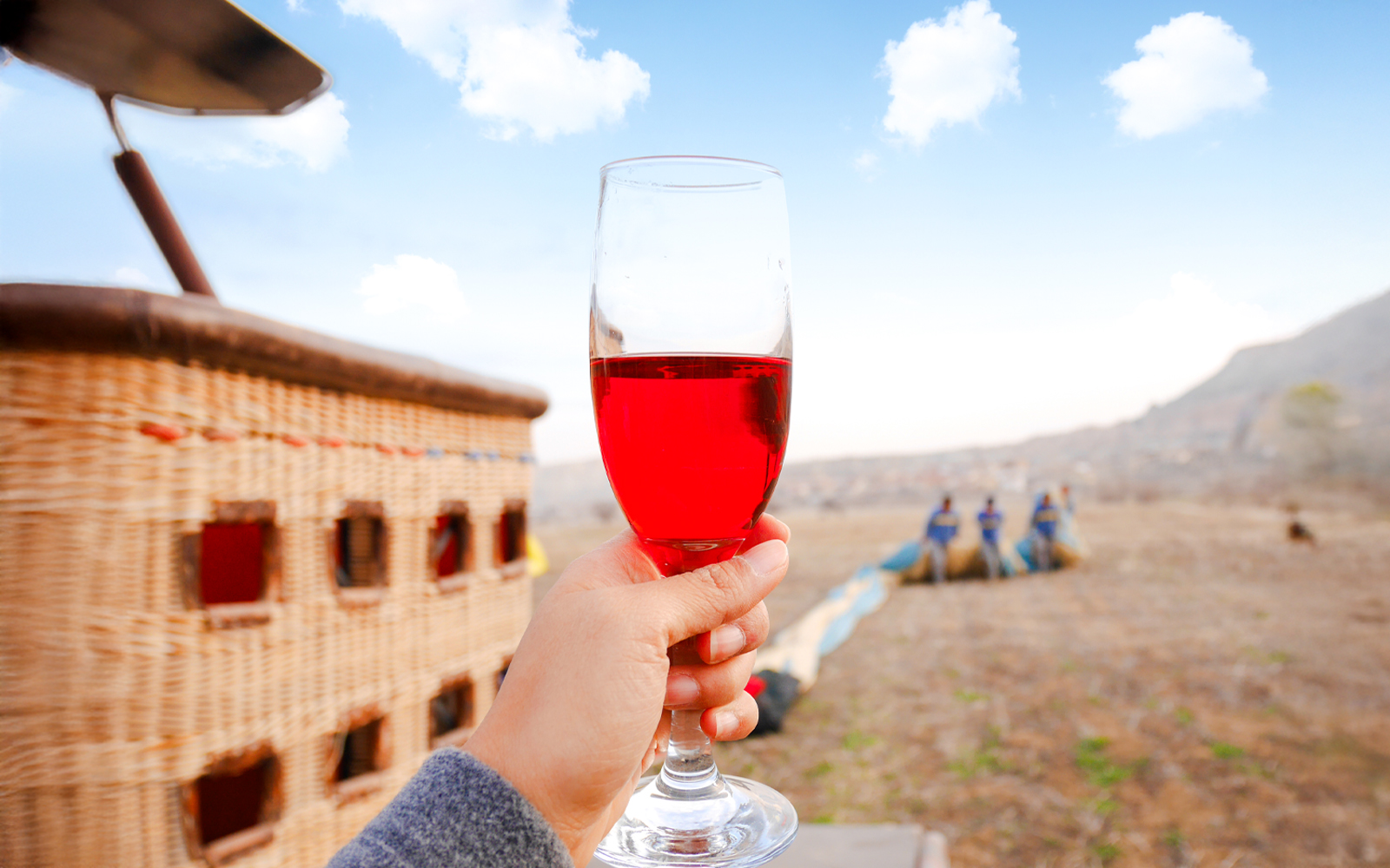 Hand holding a glass of champagne near a hot air balloon in Cappadocia, Turkey.
