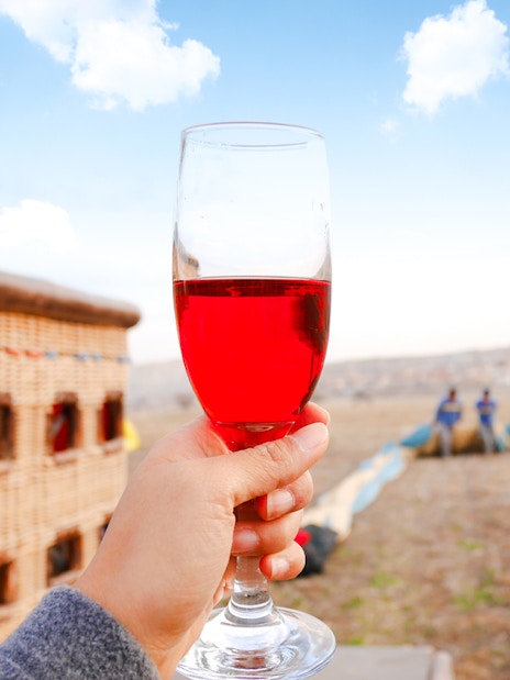 Hand holding a glass of champagne near a hot air balloon in Cappadocia, Turkey.