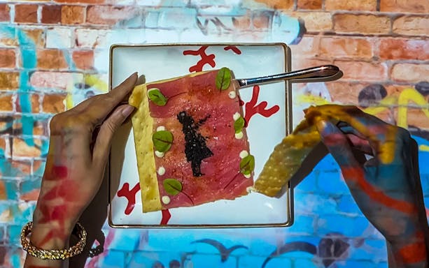 Hands holding a plate with artistic food presentation at Seven Paintings Immersive Dining Show.