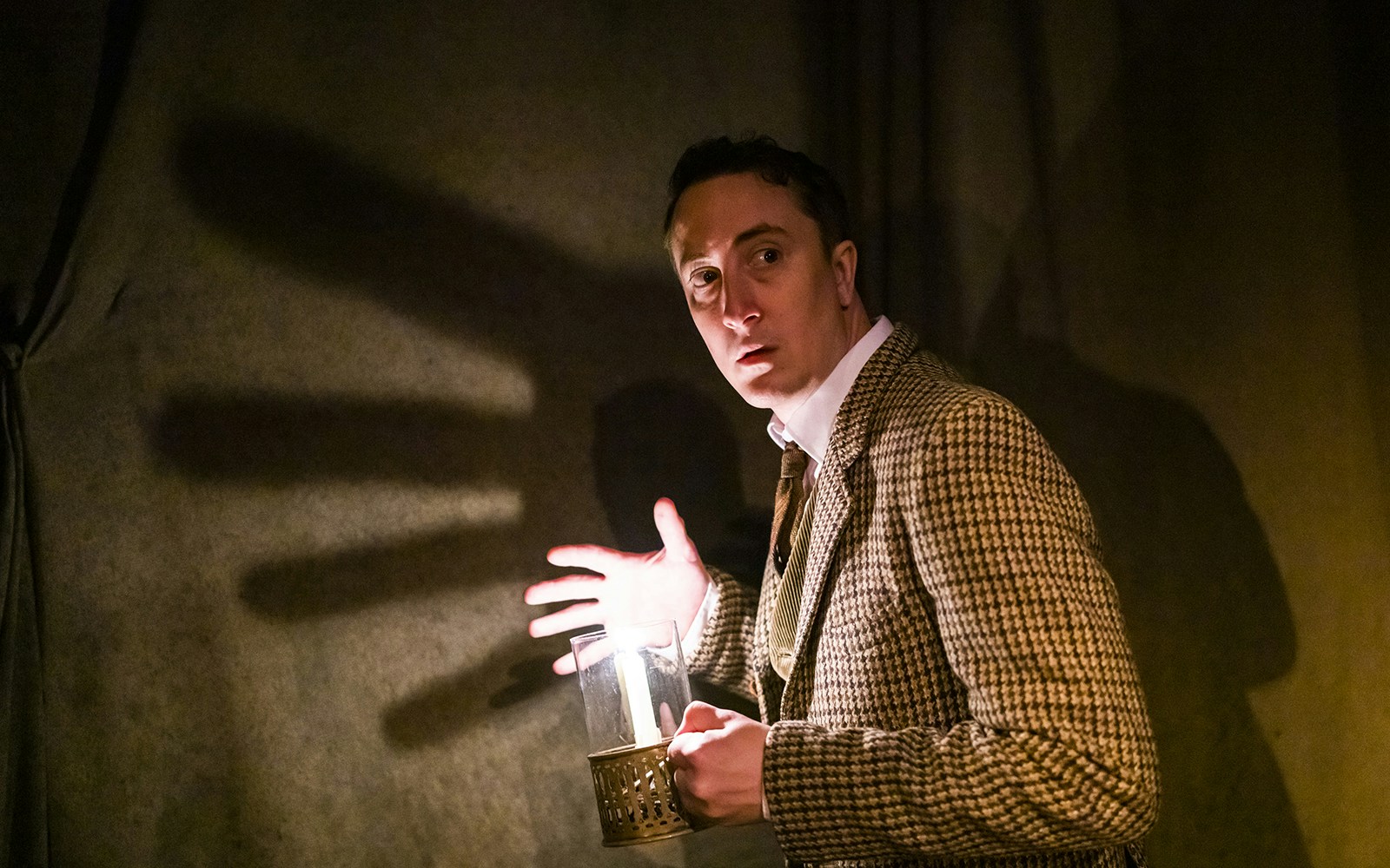 Man holding a candle with a shadow on the wall, scene from "The Woman in Black" play.